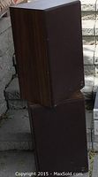 Pair of tall vintage KEF wooden cabinet speakers with front fabric grille covers shown stacked on outdoor steps.