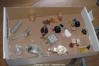 Top down view of a box containing assorted small perfume bottles of various shapes and styles including clear, frosted, and colored bottles.