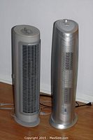 Two tower air purifiers standing side by side showing their front vents and power cords on wooden floor