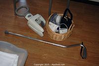 Overview of lot items on wooden floor showing walking cane, Moen grip, blood pressure monitor, headphones, and basket