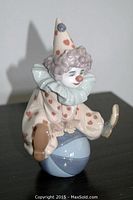 Front-left angle showing clown sitting on ball with hands on ball and foot raised