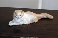 Front angle view of the porcelain cat figurine lying on a dark wooden surface, showing detailed fur and facial features.