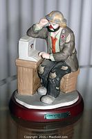 Front view of the porcelain clown figurine seated at a wooden desk with an old-style computer, on a burgundy base with a metal nameplate.