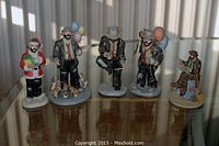 Group photo of 5 Emmett Kelly Jr. figurines on a reflective surface with curtain backdrop