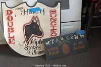 Photo showing both large white wooden sign with horse silhouette and smaller tavern sign side by side on floor