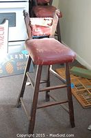 Front view showing red leather seat on black wooden barstool with carved horse head backrest, highlighting damage and usage.