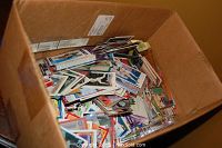 Wide angle photo of a cardboard box filled with hundreds of assorted sports trading cards in loose condition.