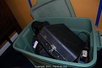Top view of green plastic tote filled with assorted camera and video equipment including Panasonic Palmcorder and cases.