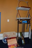 Wide shot showing metal and wood small table, spinning wheel tray, ceramic boot, blue and white metal dessert tray and red handled tin scattered around.