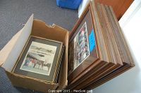 Box containing multiple framed photographs leaning against a wall, showing the quantity and condition of the lot