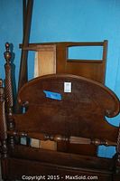 Photo of two wooden bed frames stacked against a blue wall, showing the oval-shaped headboard with turned posts and a simple rectangular footboard behind.