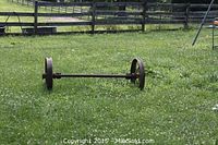 Side view of rusted axle with wheels placed on grass with wooden fence background.