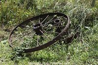 Two old rusted metal tractor wheels lying on grass, showing circular spoked design and central hub structure.