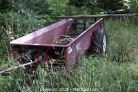 Red metal hay wagon trailer with two wheels and hitch in overgrown grass