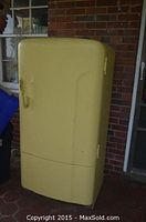 Front view of yellow retro refrigerator with visible wear and paint peeling.