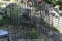 Two iron fence pieces leaning against outdoor items showing vertical bars and one with decorative curved top.