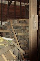 Stack of rough cut, untreated oak wood blocks arranged and stacked inside a storage area, showing wooden beam structure and some other scrap wood pieces nearby.