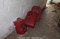 Four red plastic gas tanks lined up on the floor against a cinder block wall.