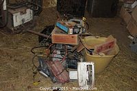 Overview of assorted power tools piled on floor, showing welder, tool box, handheld tools and cables