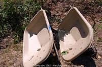 Two beige plastic Scenic Road wheelbarrows outside, showing tubs, metal frames, and missing wheels.