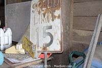 Vintage metal Speed Limit 15 sign positioned behind other items on a shelf.