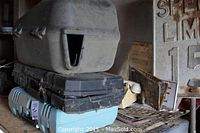 Stacked plastic tool cases including a large textured gray case, two black cases and a blue case, stored on a shelf in a workshop.
