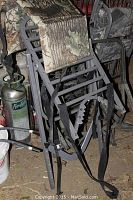 Pair of aluminum frame deer stands standing upright showing camouflaged fabric seats and adjustable supports