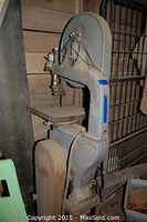 Photo of the large metal band saw showing the main body and cutting table with rust and wear visible.
