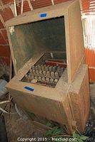 Full view of large metal chicken plucker showing rusted metal housing with an open top.