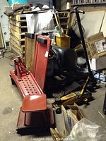 Photo shows multiple red mechanic creepers stacked alongside a black padded creeper, a yellow hydraulic trolley jack, and some red metal jack stands in background.