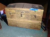 Front view of round top wooden travel trunk showing metal reinforcements and leather handle.