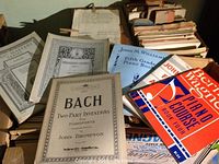 Collection of old music lesson books and sheet music including Bach Two-Part Inventions and multiple piano course books.
