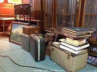 Overall lot showing vintage books, portable typewriter case, rolling cart, framed wall art, and other vintage items on a carpeted floor against wooden furniture.