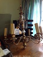 Full view of brass chandelier with five candle-style light sockets and ornate arms.