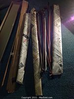 Multiple wooden bass bows wrapped in newspaper and cardboard laying on carpeted floor.