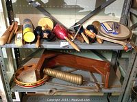 Wide angle view of various percussion instruments on metal shelving including wood blocks, maracas, tambourine, triangle, and claves.