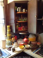 Wide view of kitchen counter and open cabinet interior showing plastic canisters, glass bowls, metal strainer, and ceramic bowls.