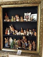 Full view of shadow box containing multiple colorful ceramic figurines of musicians and musical instruments on three shelves with an ornate gold frame.