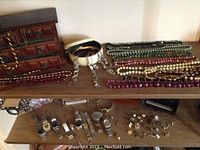 Top shelf with carved wooden multi-drawer jewellery box, ivory bangle bracelet, silver-tone chandelier earrings, assorted beaded pearl necklaces in green, maroon, purple, white.