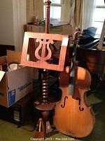 Photo of vintage wooden music stand with carved lyre holder, standing next to a decorative wooden cello.