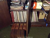 Multiple vinyl records stored vertically in two wooden cabinets; leather-bound cassette albums placed on wooden box in front.