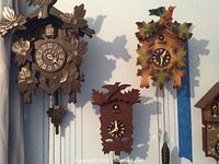 Three wooden cuckoo clocks hanging on a wall with visible details of clocks and chains.