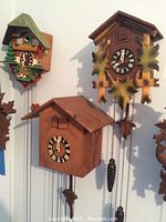 Three wooden cuckoo clocks mounted on a white wall showing decorative details and clock faces.