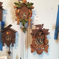 Three cuckoo clocks hung on wall, showing different carved and painted bird and leaf motifs