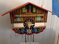 Front view of chalet style cuckoo clock with painted floral decoration and figurine