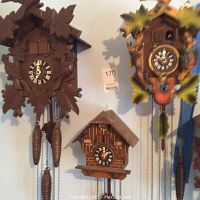 Photo showing all three cuckoo clocks hung on a wall, visible details of dial faces and pendulum chains