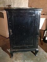 Front view of black painted wooden music cabinet with one door and visible surface wear and scratches