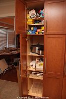 Full view of kitchen cabinet with open doors showing all items stacked inside on shelves: crock pots, boxes, rolls, and other supplies.
