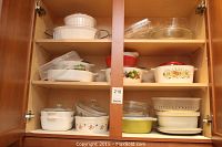 Two wooden cupboards filled with ceramic, glass and plastic baking dishes and bowls, some with floral decoration.