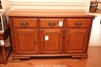 Front view of the wooden colonial style sideboard showing 3 cupboard doors and 2 drawers with decorative brass-colored handles and knobs.